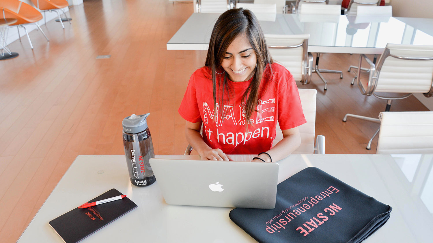 Girl working on her laptop wearing a "Make it happen" shirt in Hunt library.