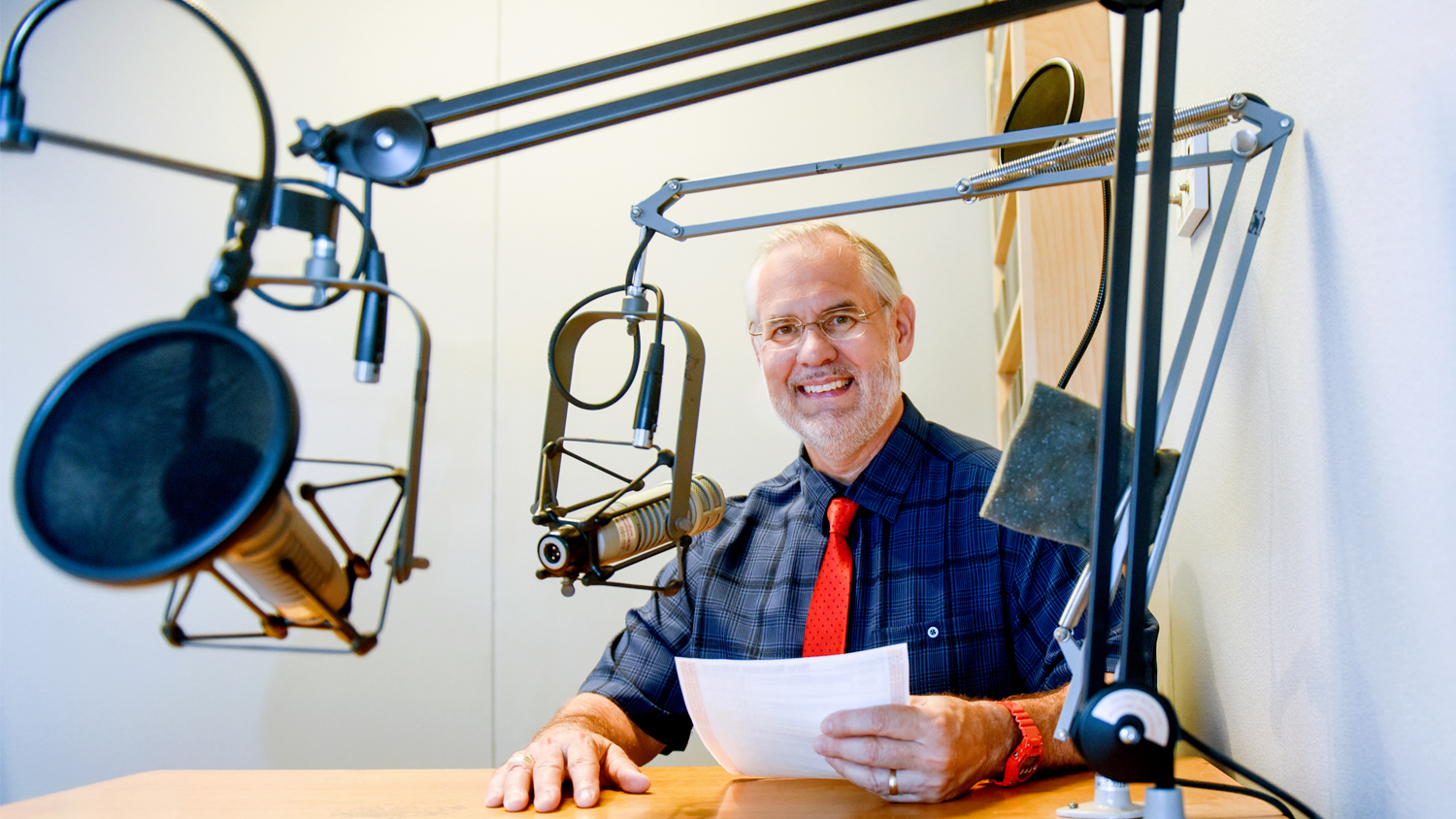 Man smiling in front of podcast microphone while holding notes