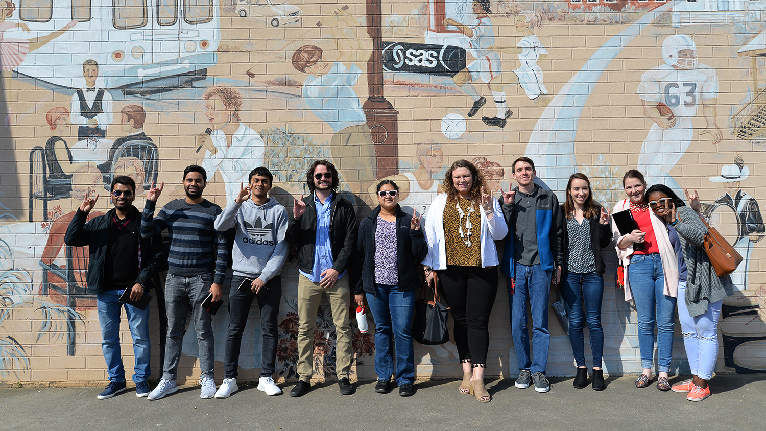 Albright Entrepreneurs Village students pose with wolf signs by the mural in downtown Cary.