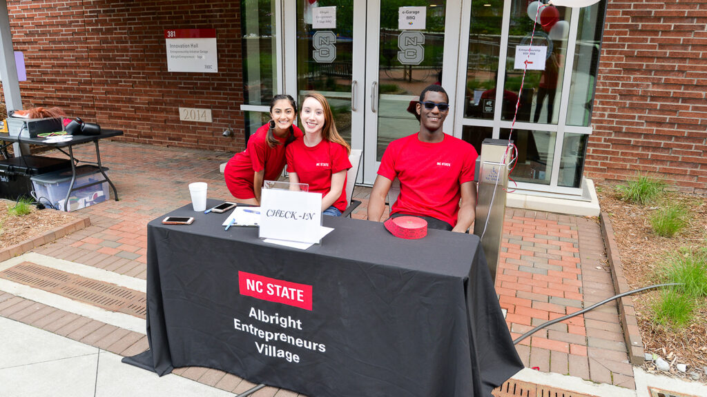 eGarage and Albright Entrepreneurs Village student employees smiling while running the check-in table at the end-of-year barbecue.