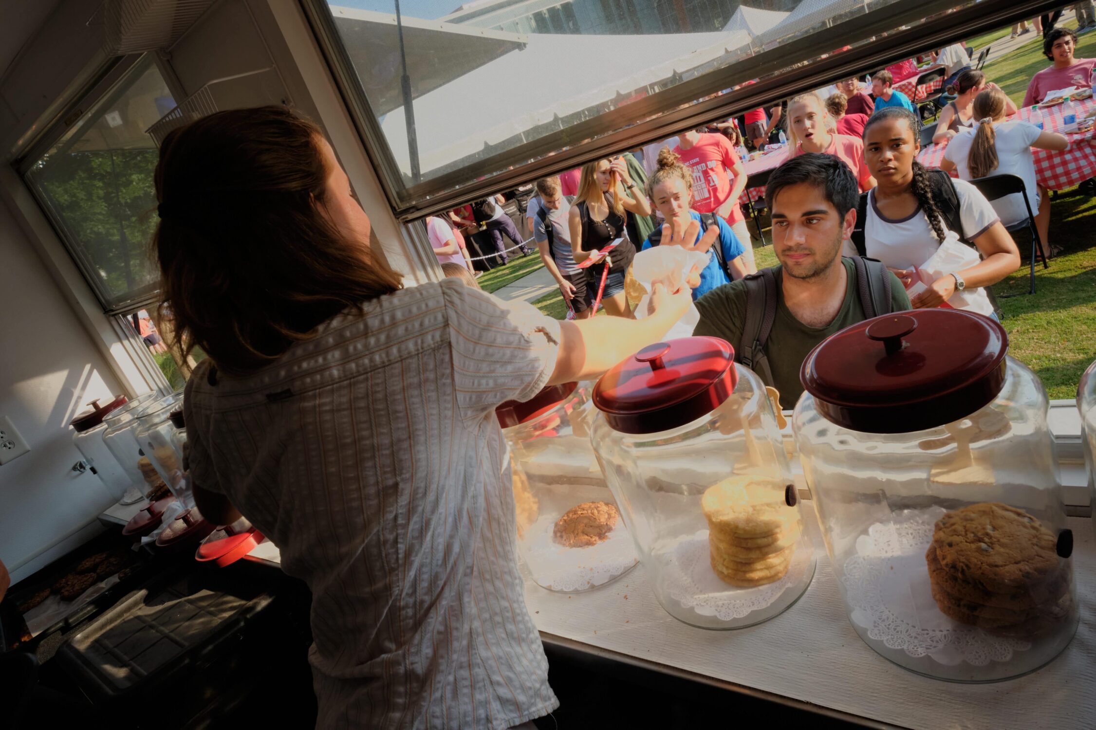 woman handing out cookies to students at cookie booth