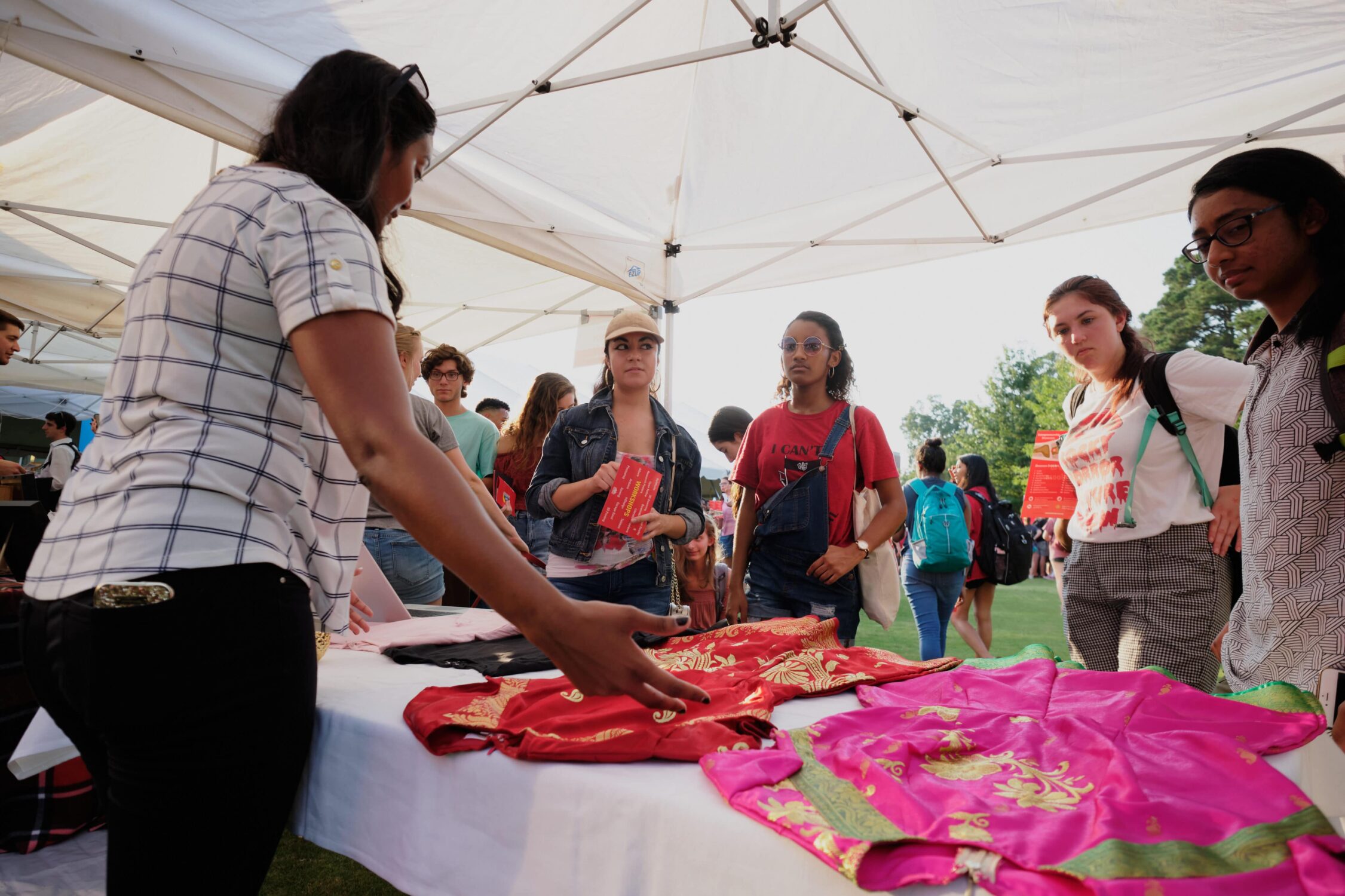 woman showing cultural clothing to students at her booth