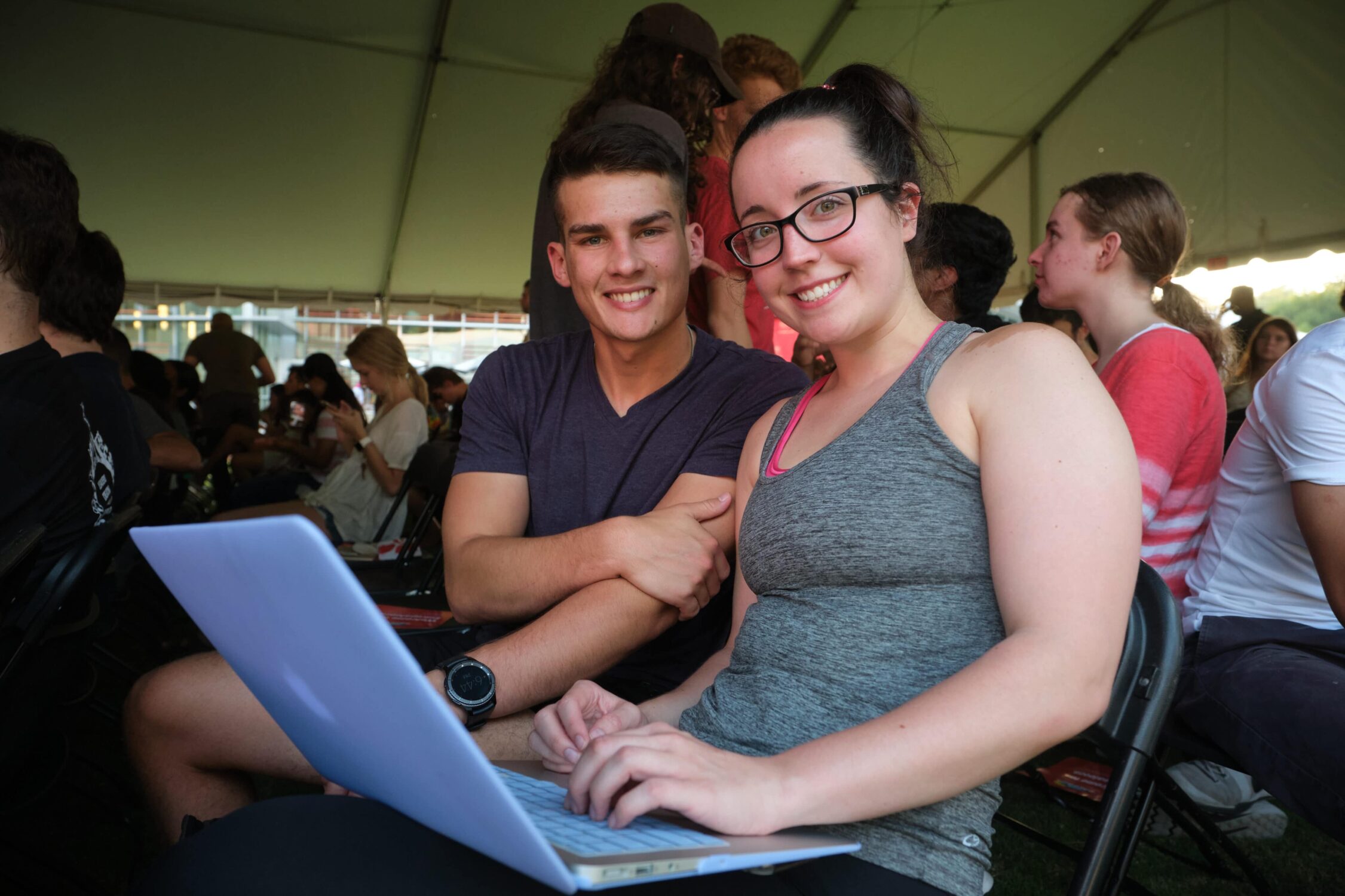 male student smiling while girl student smiles next to him with laptop in her lap.