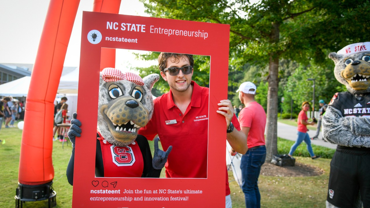 NC State entrepenrship ambassador posing with Mrs. Wuf at outdoor festival