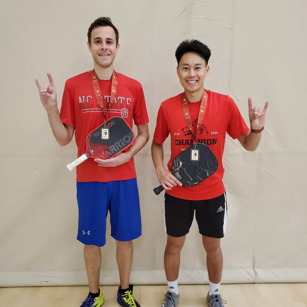 Two pickleball players with paddle holding their hands in Wolfpack sign