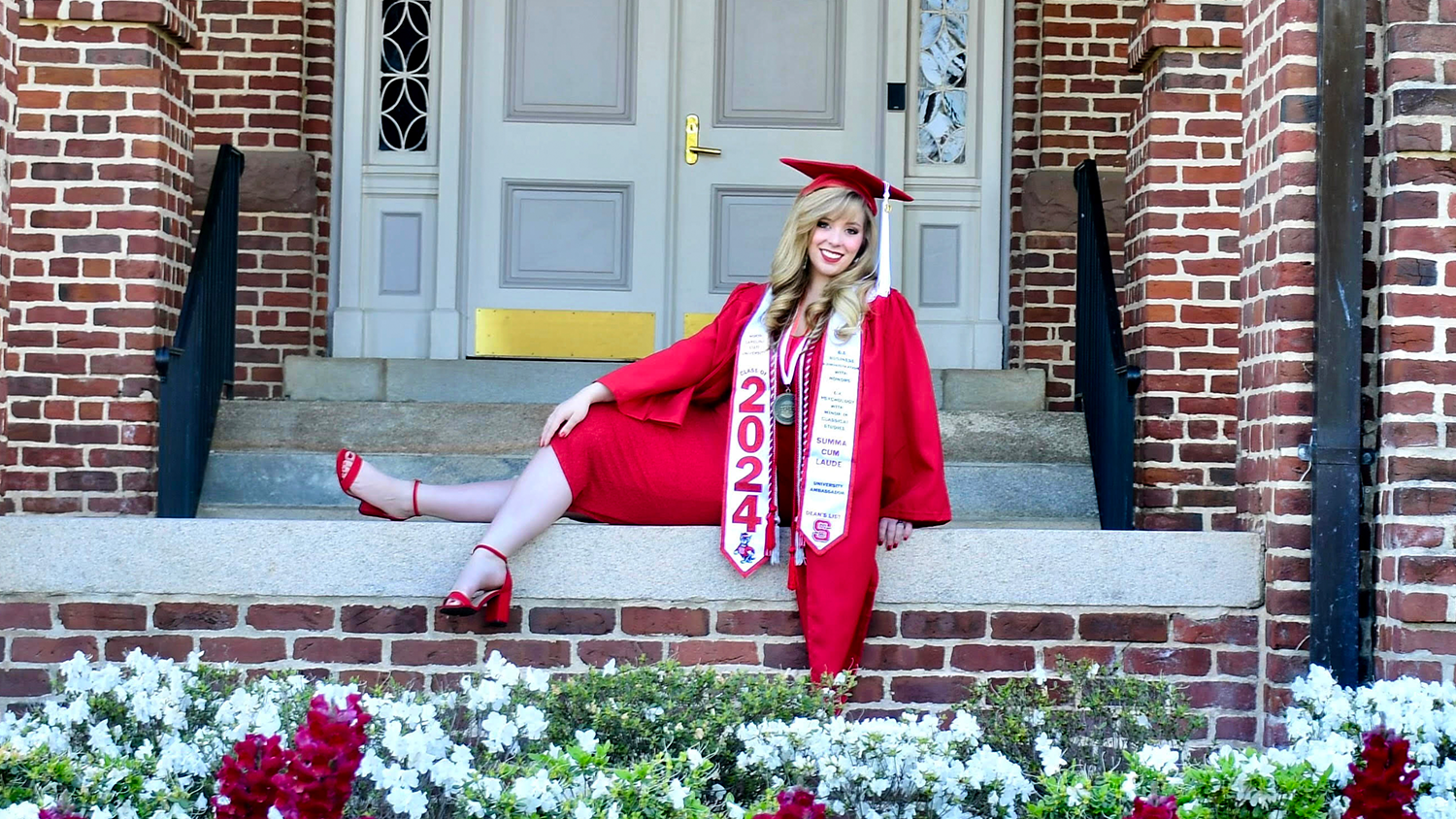 student in cap and gown in front of brick building