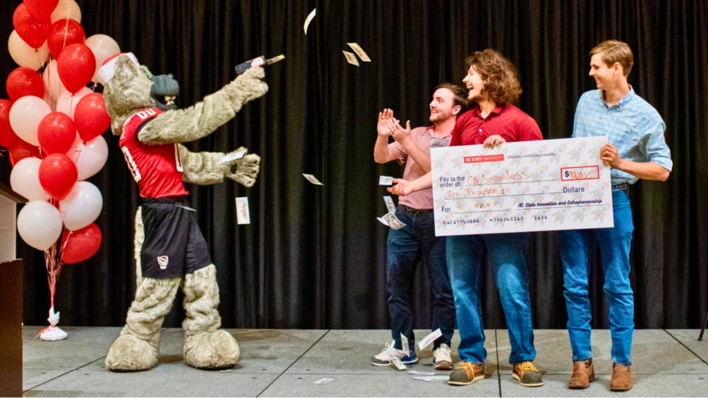 Mr. Wuf and 3 students holding a large check 