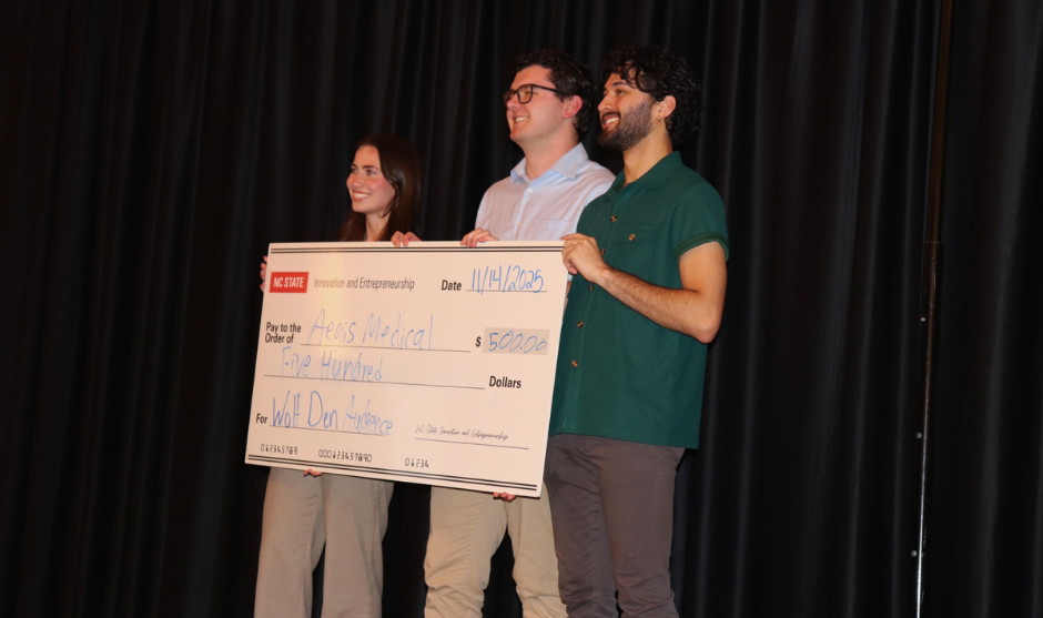 Three people holding a large sign posing for a picture.